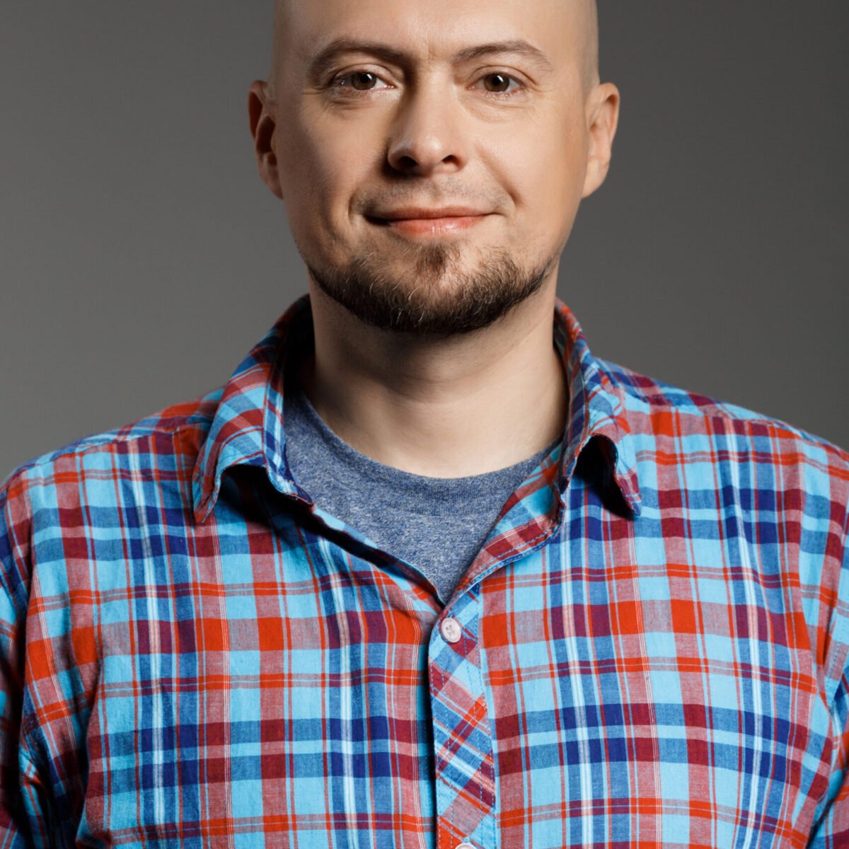 Portrait of cheerful handsome middle-aged man in plaid shirt looking at camera smiling over grey background. Copy space.